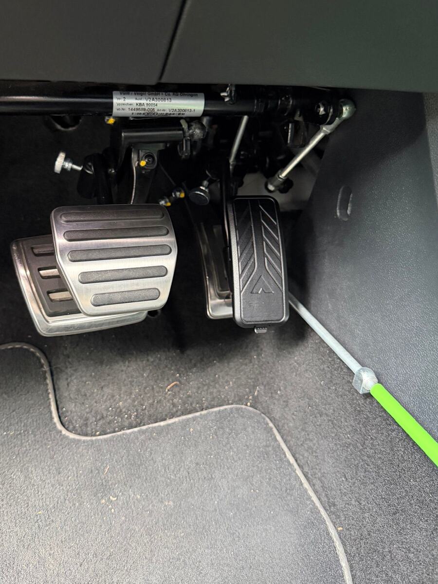 Fußraum eines Fahrschulautos mit Pedalverlängerung: Auf Kupplung
                                  und Bremse sitzen große Metallauflagen, über dem Gaspedal ein
                                  zweites, aufgesetztes Pedal. Unter dem Armaturenbrett verläuft
                                  eine Achse, von der Gestänge zu den Pedalen führen